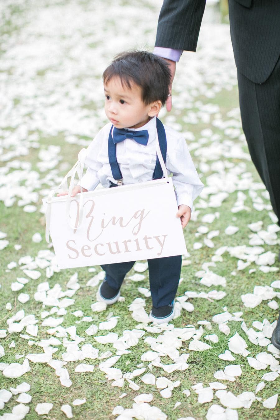 Ring Security ring bearer in blue bowtie and suspenders walking down wedding ceremony aisle | Photography: Jada Poon Photography via Style Me Pretty