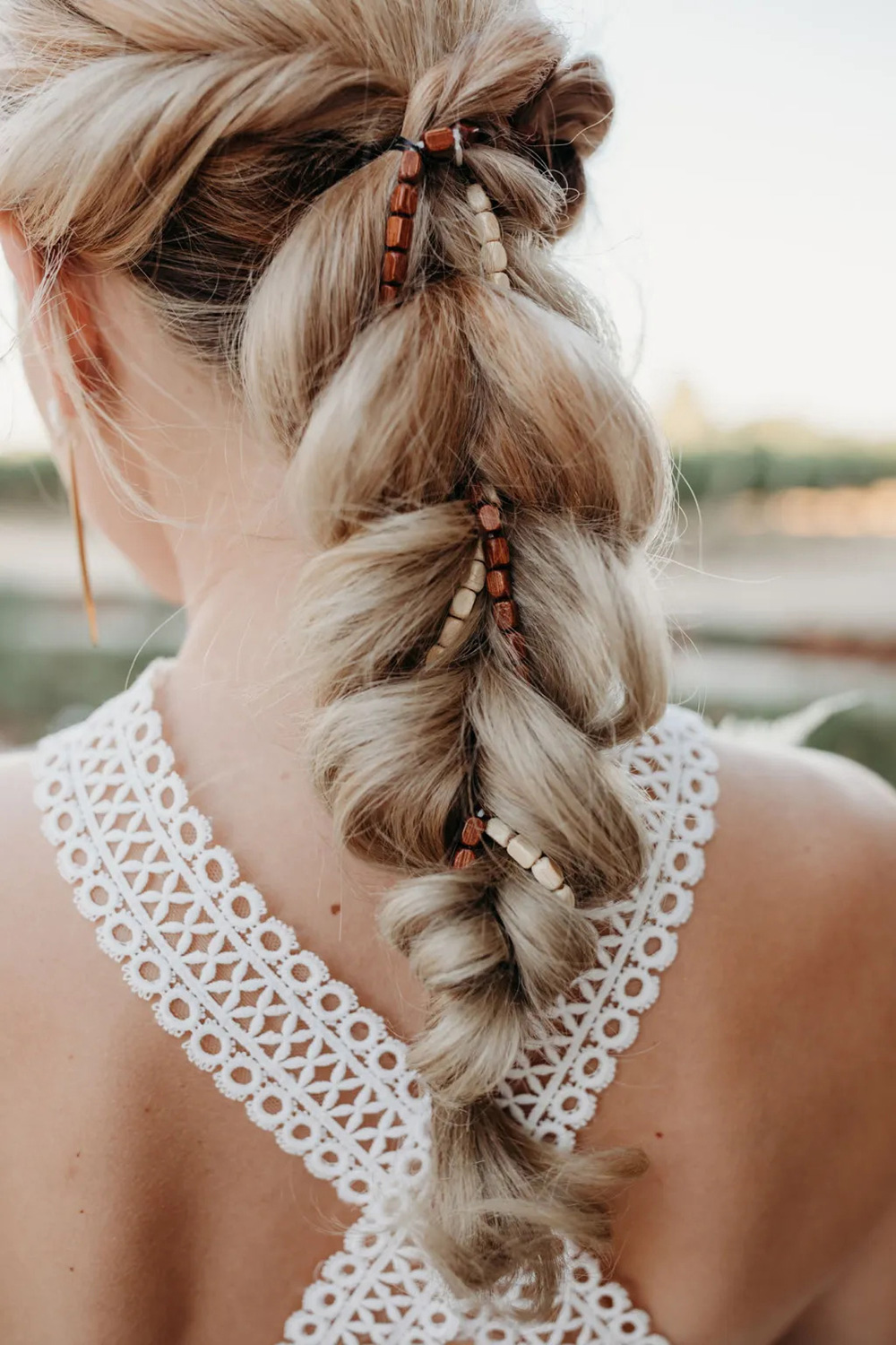This romantic boho wedding hairstyle features a loose braid ponytail adorned with brown and ivory wooden beads woven through. A stunning look for bride or bridesmaids! | Liz Koston Photography via Green Wedding Shoes