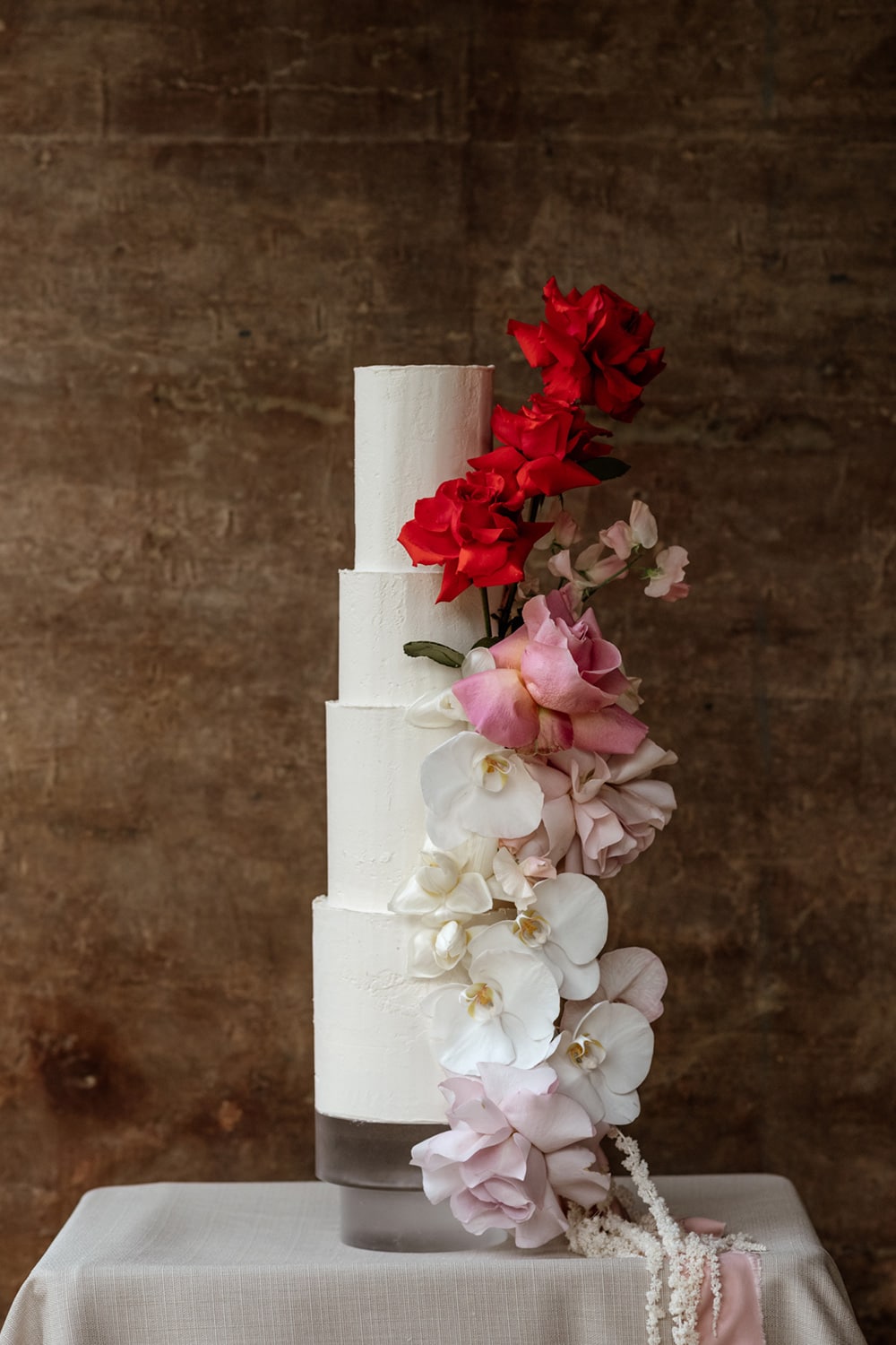 Modern Red & Pink Wedding Ideas | An elegant four tier wedding cake in white buttercream topped with cascading ombre florals in red, pink and white, including roses, orchids, sweet pea and amaranthus. | Photography: Laura Martha Photography via Bridal Musings