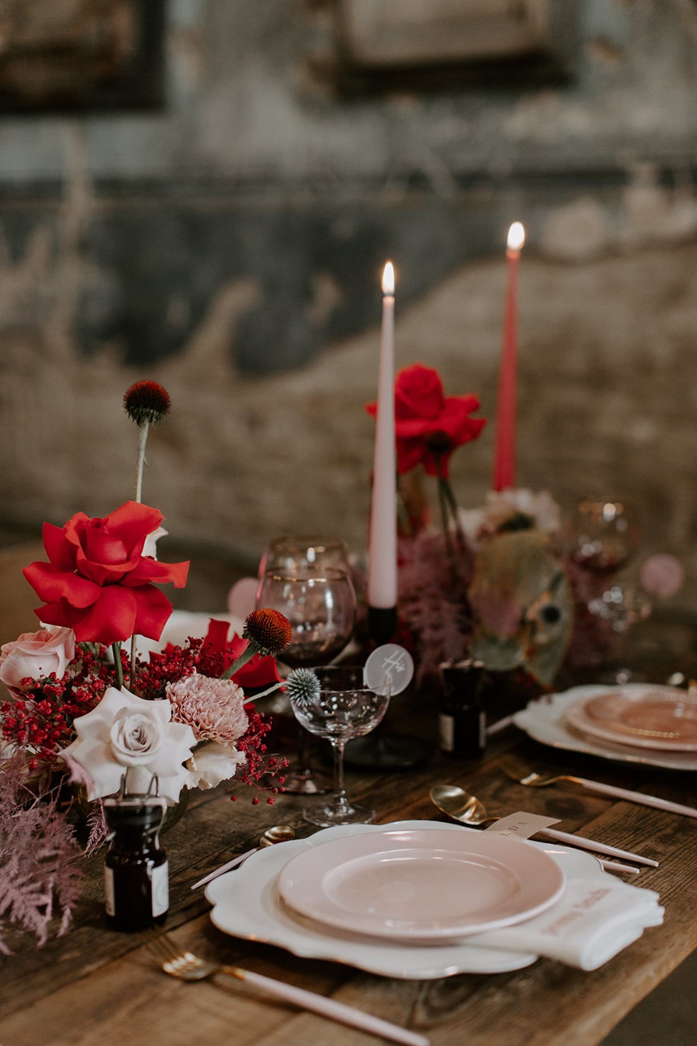 Modern Red & Pink Wedding Ideas | A modern industrial wedding reception table setting on a bare wood table features layered blush and white tableware, artful red and pink flower arrangements and tonal taper candles to match. | Photography: Emily Rose Photography via The Stars Inside