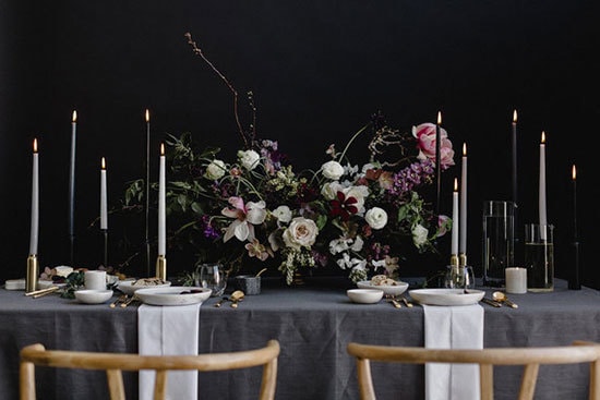 Moody botanical wedding reception table setting with grey linen, centrepiece featuring white, pink and purple flowers and candlesticks on a black backdrop | A Sea of Love via 100 Layer Cake