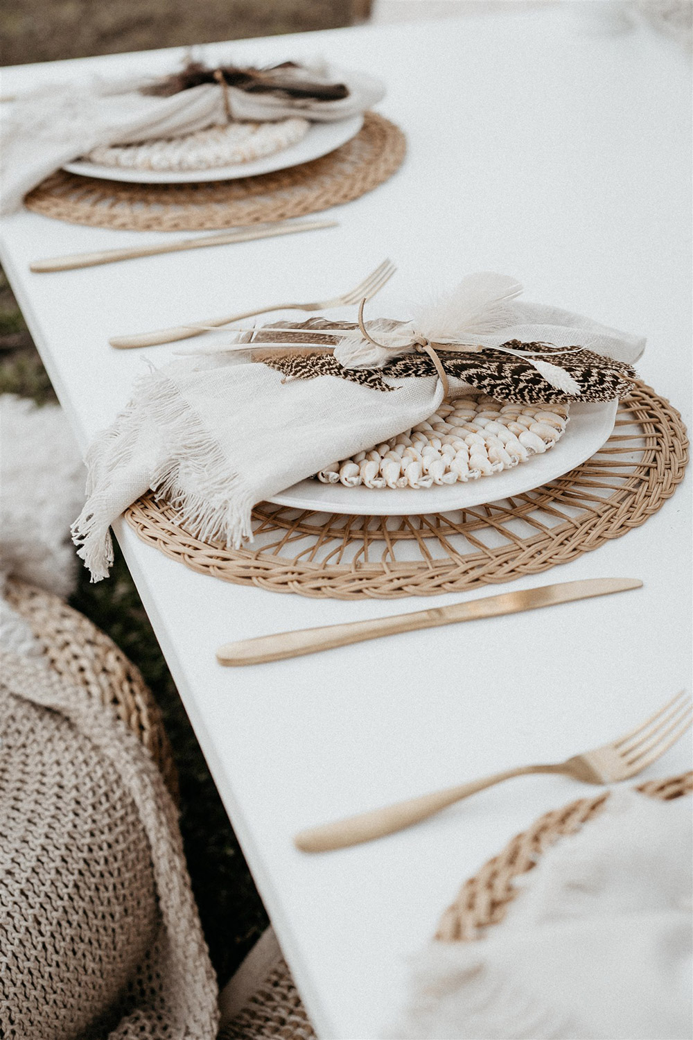 Outdoor Festival Bohemian Wedding Inspiration | The place settings feature gold cutlery, a natural woven placemat topped with white plateware and neutral napkins tied with cord and feathers. | Photography: Shae Estella Photo