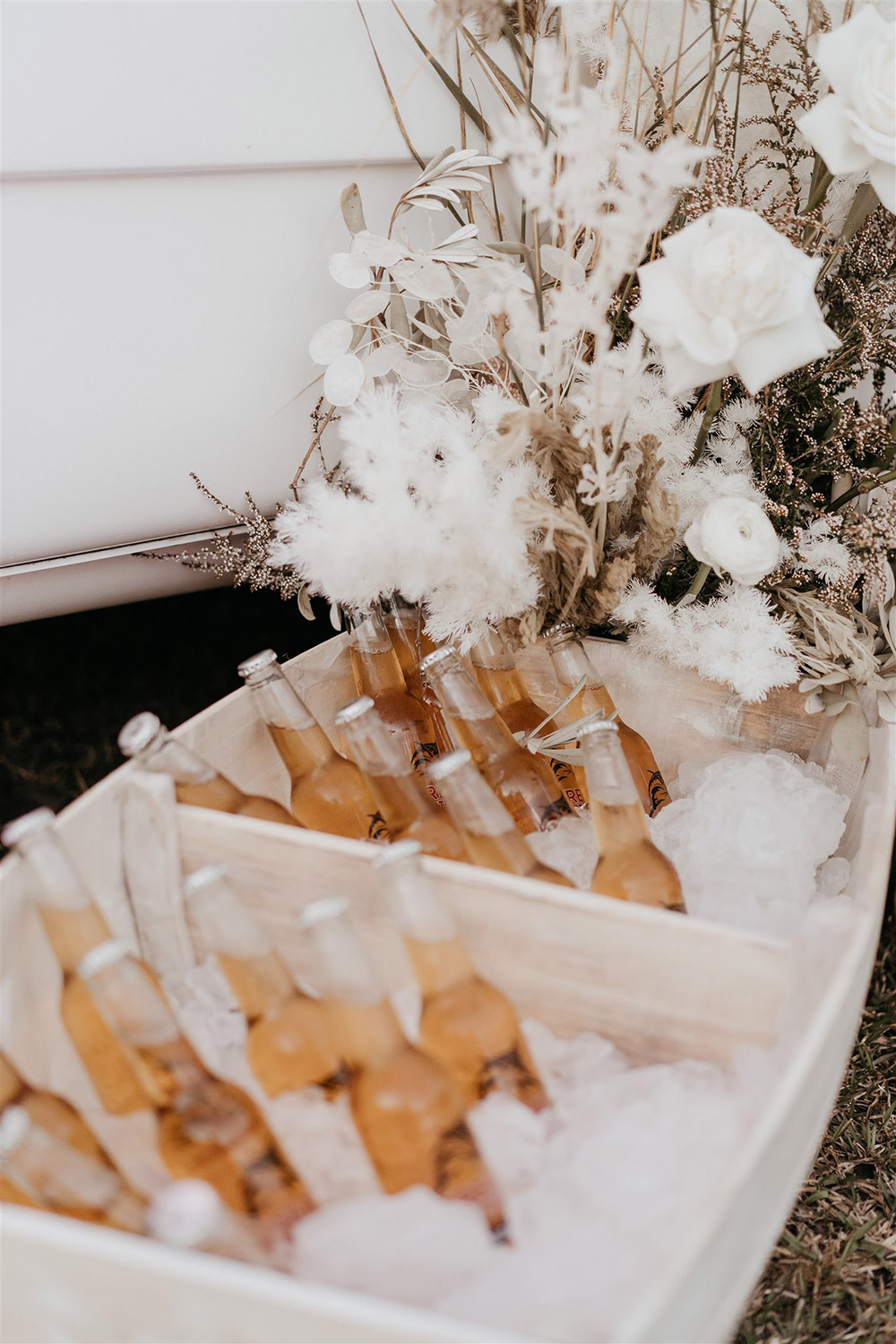 Outdoor Festival Bohemian Wedding Inspiration | After the wedding ceremony, guests are served drinks from a white vintage caravan bar and miniature row boat filled with beer on ice. This setting is styled with white and neutral floral arrangements to match the rest of the boho wedding decor. | Photography: Shae Estella Photo