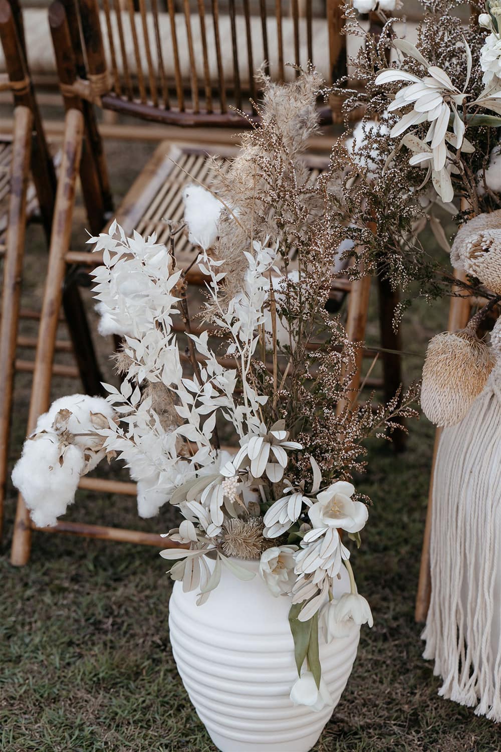 Outdoor Festival Bohemian Wedding Inspiration | This outdoor boho wedding ceremony consists of woven jute rugs for the aisle and two pillars of white circles in varying sizes adorned with macrame, feathers and flowers for the arbour. The setting is framed by bamboo folding chairs for guests and large white vases decorated with fringed macrame wraps that are filled with neutral dried floral arrangements accented with stems of white tulips, stocks, cotton and ruscus. | Photography: Shae Estella Photo