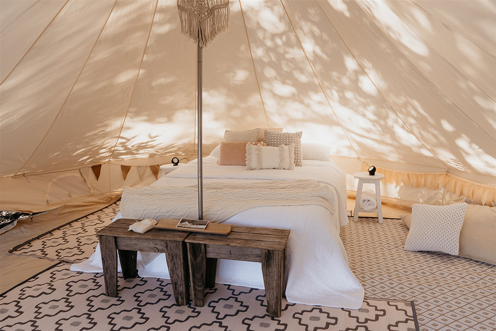 Outdoor Festival Bohemian Wedding Inspiration | A bronze, neutral and white balloon installation frames the entrance to the couple's glamping tent, styled with layered bohemian rugs, throw pillows, a queen bed, camp chairs, fabric garlands, wooden furnishings and wicker decor. | Photography: Shae Estella Photo