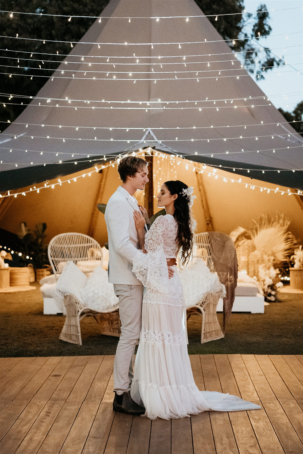 Outdoor Festival Bohemian Wedding Inspiration | This loved-up couple shares their first dance on a timber dance floor beneath a canopy of twinkling fairy lights and in front of a large tipi styled with eclectic lounge seating. | Photography: Shae Estella Photo