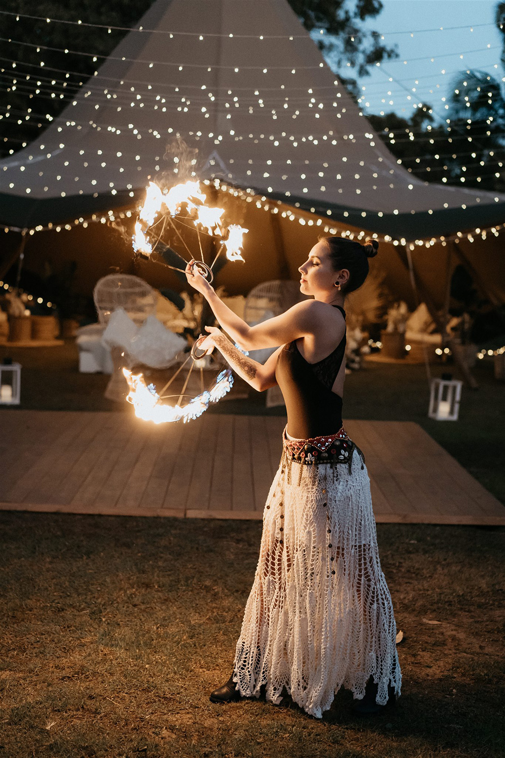 Outdoor Festival Bohemian Wedding Inspiration | A fire twirler performs as wedding entertainment in front of a canopy of fairy lights and large tipi styled with eclectic lounge seating for an outdoor boho wedding reception. | Photography: Shae Estella Photo