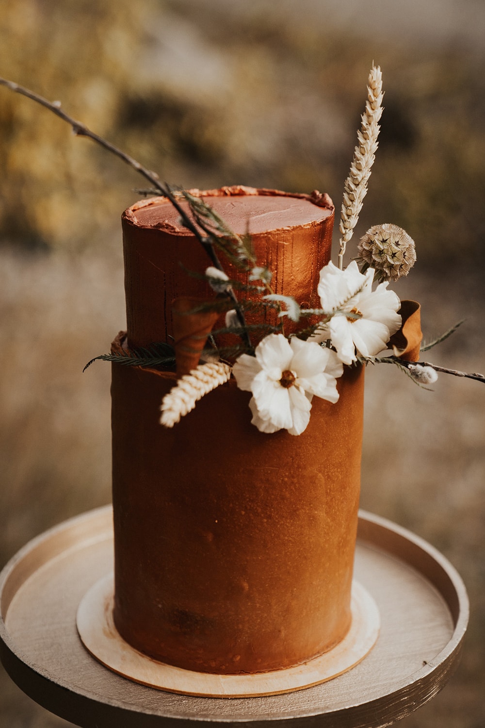 Boho Rust & White Wedding Ideas |  Tall rust coloured two tiered buttercream wedding cake with a small arrangement of rustic white and dried flowers between the first and second tier. | Photography: Anna Tee Photography via Storyboard Wedding