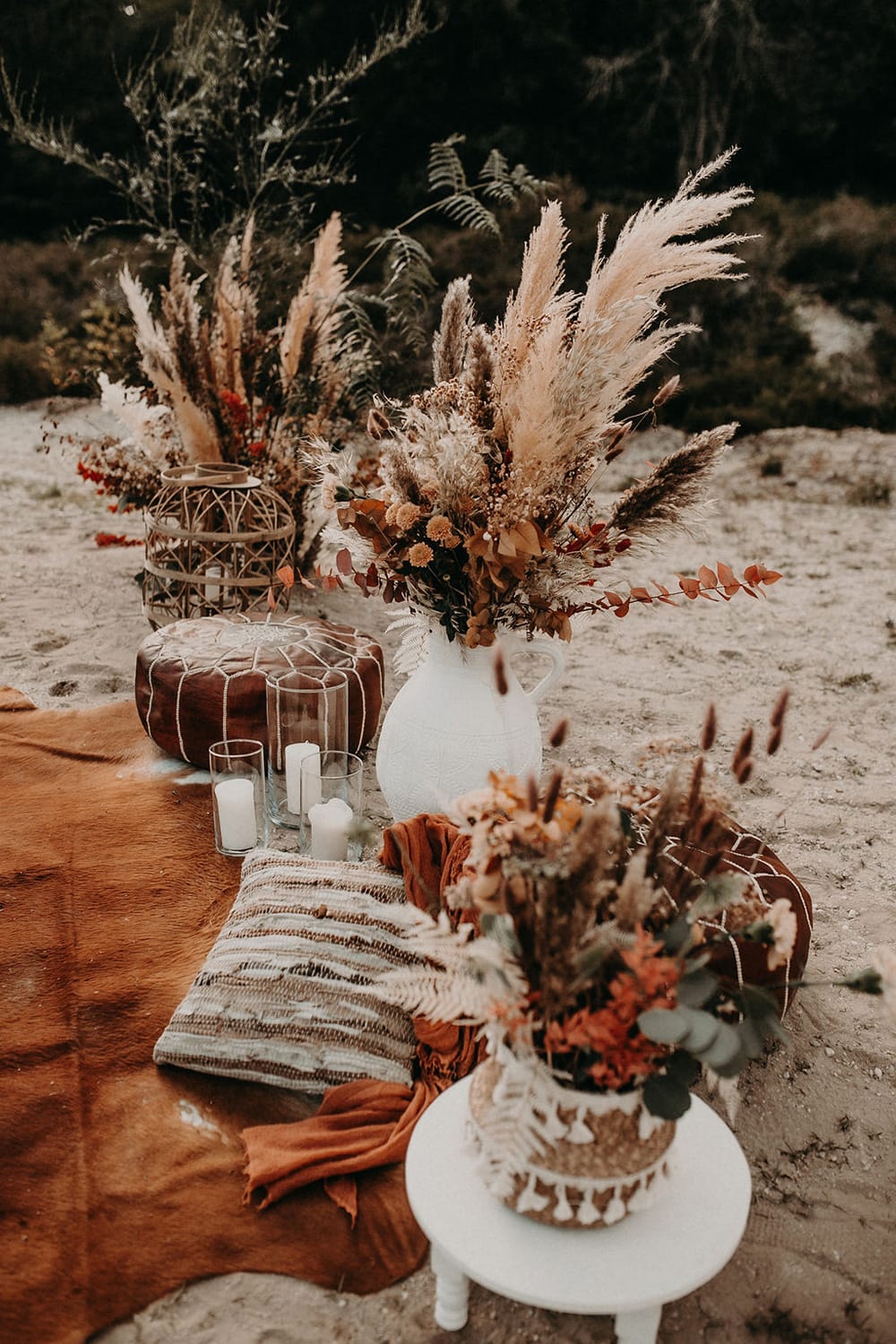Boho Rust & White Wedding Ideas | Create a relaxed outdoor wedding seating area with a rust coloured rug, scattered floor cushions, white pillar candles in glass hurricane vases, large bamboo lantern, white low set table and earthy dried flower arrangements in eclectic vessels featuring wild pampas grass. | Photography: Mel Ende Photography