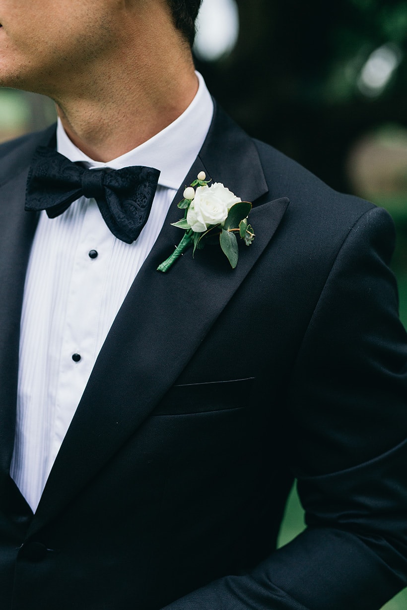 Modern groom wearing black suit, bow tie and white rose buttonhole | Figtree Wedding Photography